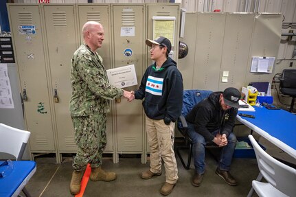 Capt. Jip Mosman, commander, Puget Sound Naval Shipyard & Intermediate Maintenance Facility, congratulates Tracy Hartz, work leader, Shop 26, Welders, during a Bravo Zulu award ceremony May 27, 2022 at PSNS & IMF in Bremerton, Washington. Hartz, who started as a PSNS & IMF helper-trainee eight years ago, suggested cutting away a much smaller portion of the reboiler tank to access the tubing inside. This suggestion eventually resulted in an estimated 4,400 labor hours saved — every time the team does this job. (U.S. Navy photos by Scott Hansen)