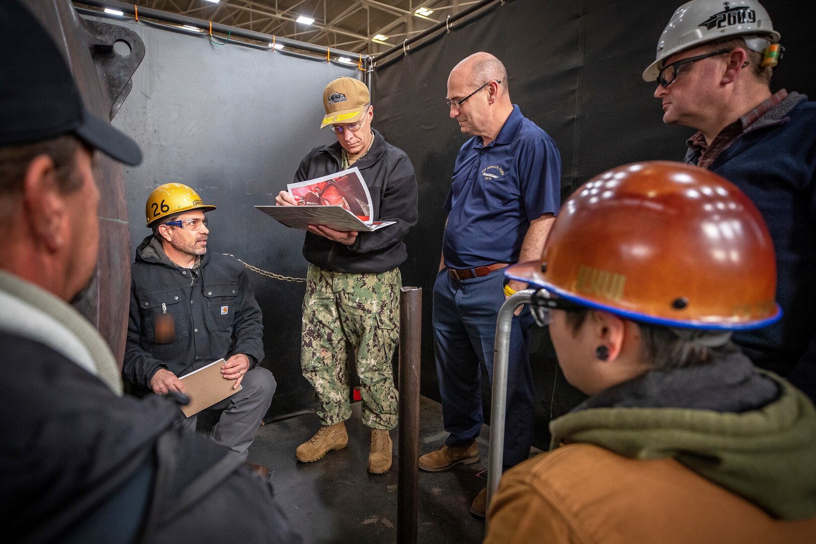 Tracy Hartz, lower right, work leader, Shop 26, Welders, listens as Ronald Cenicola, left, Non-Nuclear director, Shop 26, briefs Rear Adm. Jason Lloyd, middle, Chief Engineer and Deputy Commander of Ship Design, Integration and Naval Engineering, NAVSEA 05, and Doug Vaughters, right, CVN Design and System Engineering Director for NAVSEA 05, on Shop 31 operations during a tour March 31, 2022, of Puget Sound Naval Shipyard & Intermediate Maintenance Facility in Bremerton, Washington. (PSNS & IMF photo by Scott Hansen)