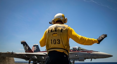 Aviation Boatswain's Mate (Handling) 3rd Class Jihad Lake assigned to the Nimitz-class aircraft carrier USS George H.W. Bush (CVN 77) signals an F/A-18E Super Hornet, attached to Strike Fighter Squadron (VFA) 136, before launch, June 20, 2022.