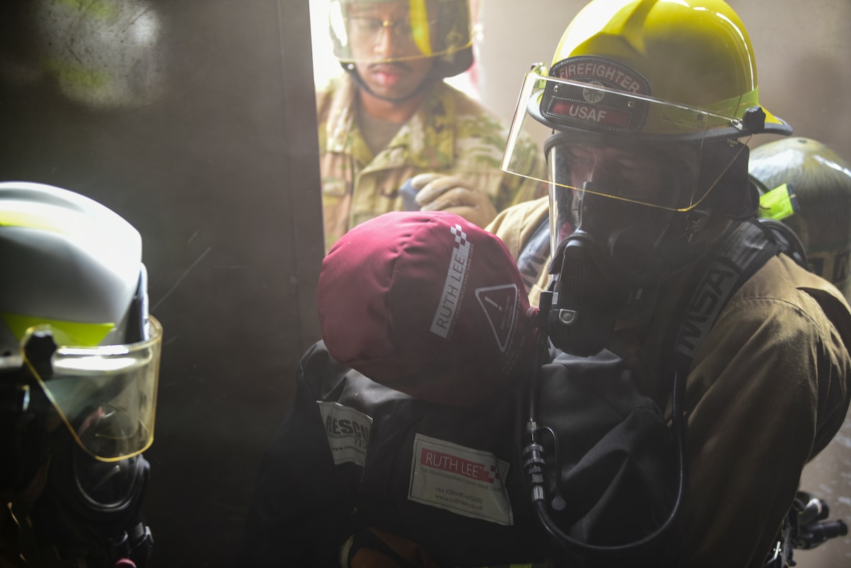 a photo of firefighters carrying a manikin out of a building
