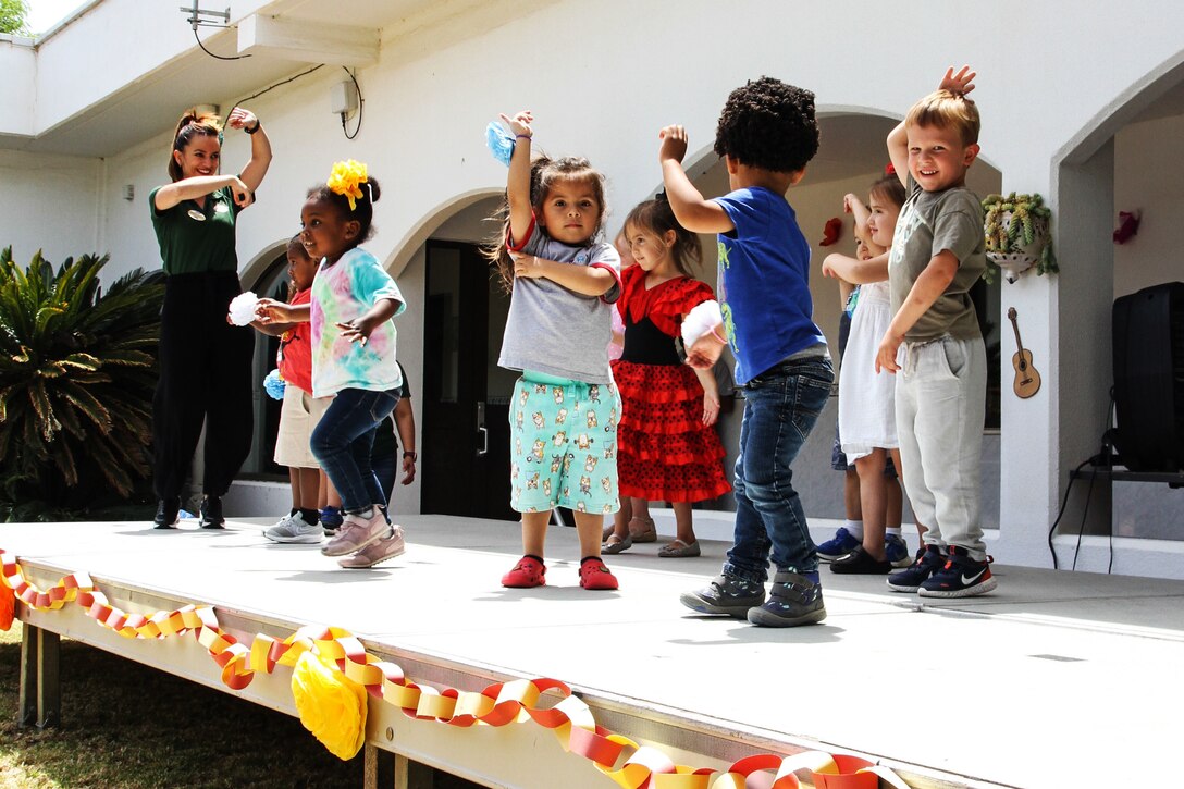 Children dance on a decorated stage outdoors with an adult.