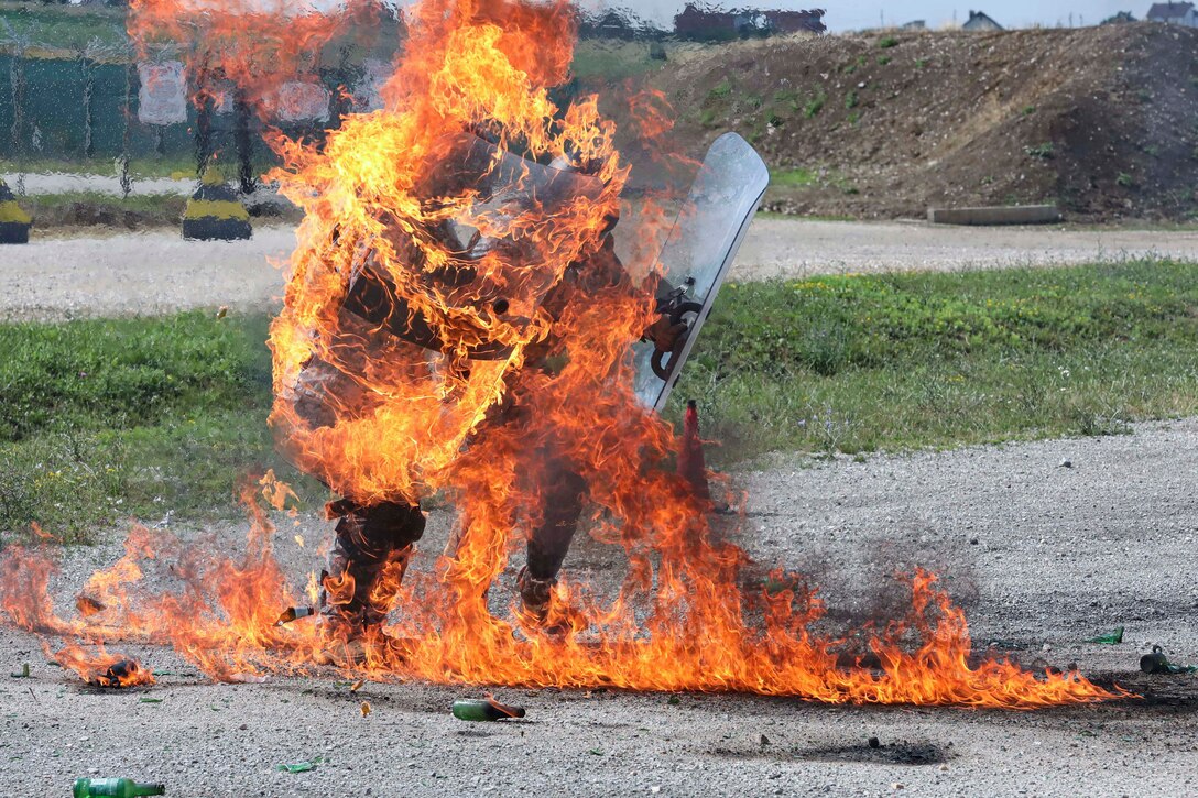 A service member holding two shields catches fire during training.