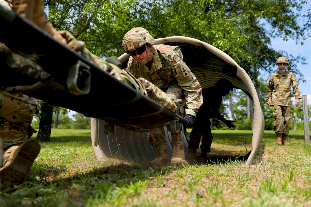 A solider carrying a stretcher moves through an obstacle.