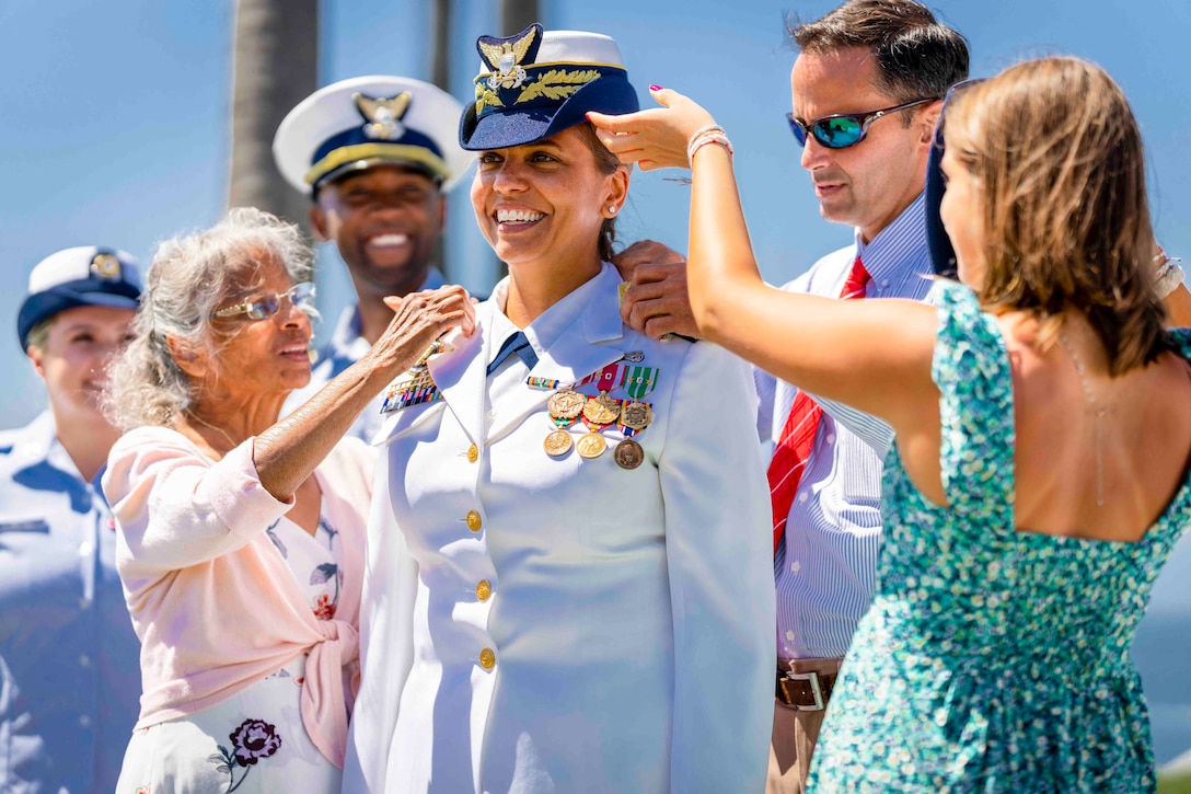 Three people adjust the uniform of a sailor as others watch.