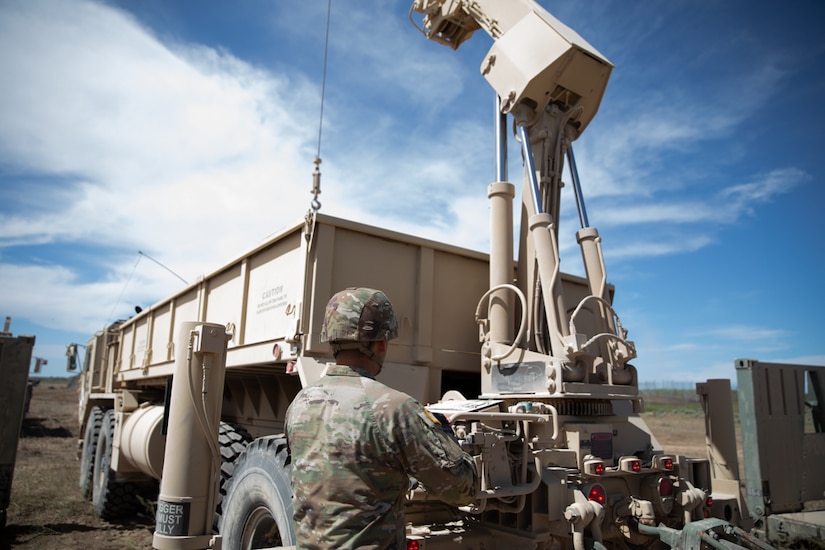 A soldier works with a crane on the back of a military vehicle