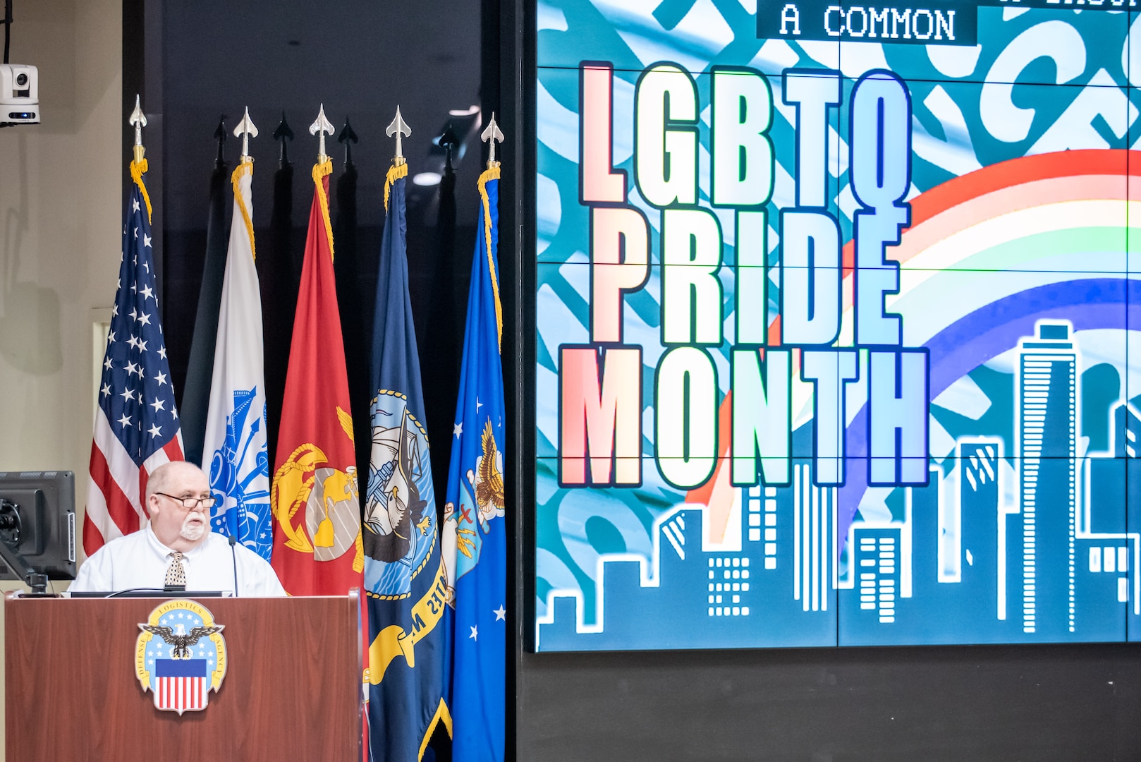 A man in a white shirt speaks at a podium on stage.