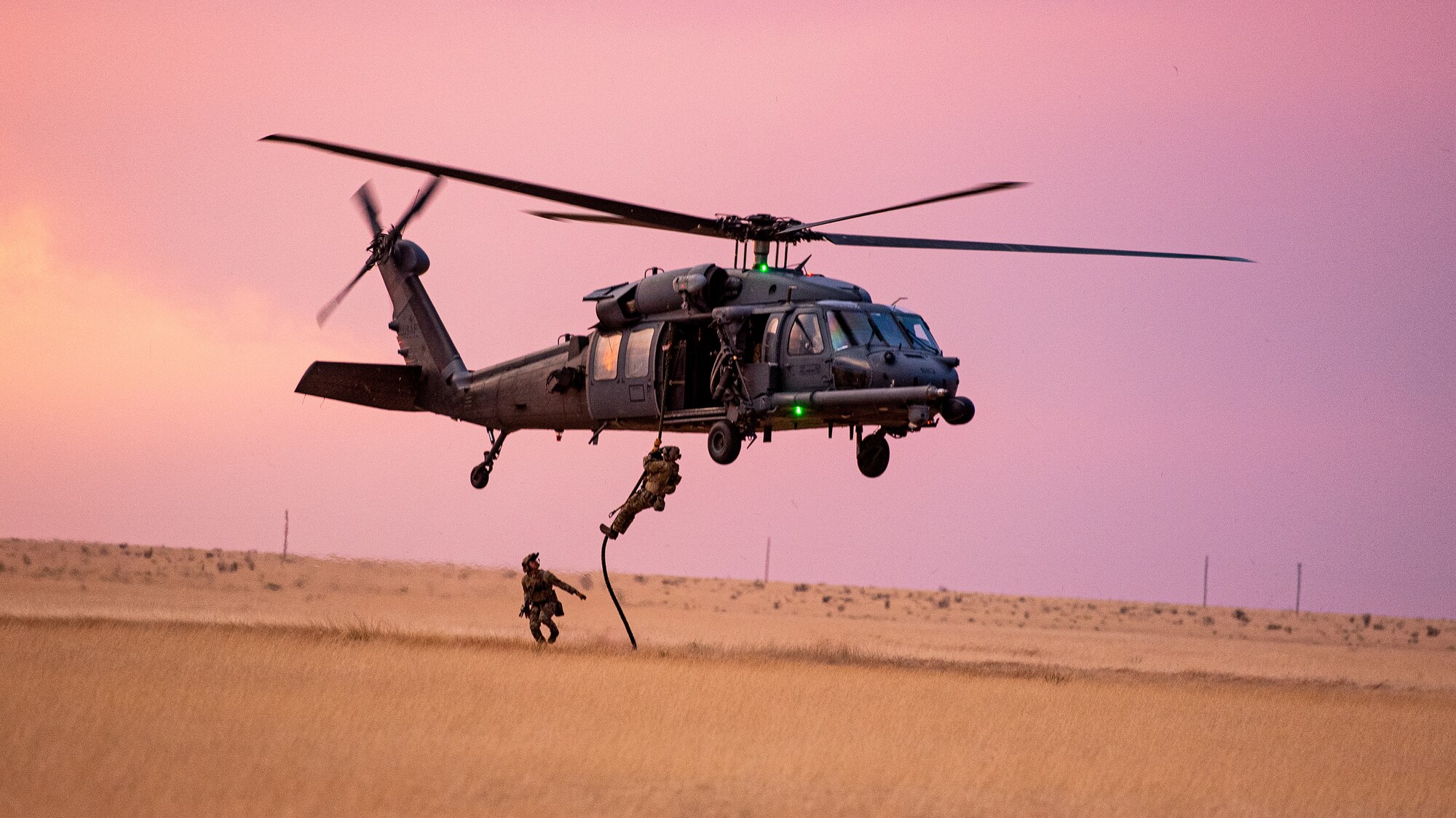 Airmen slide down a rope to the ground from a helicopter.