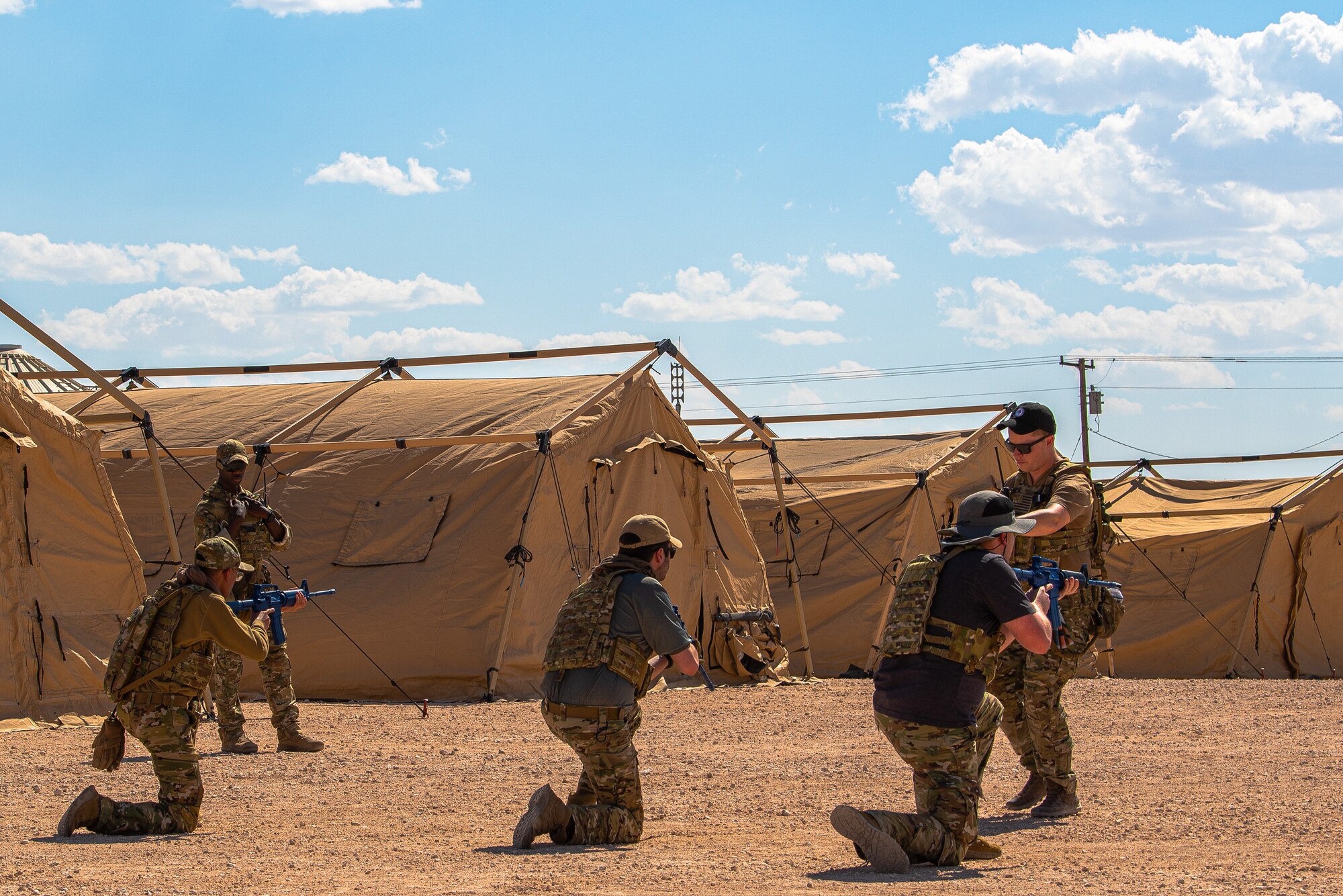 Three Airmen kneel and point rifles straight ahead while an instructor speaks to them.