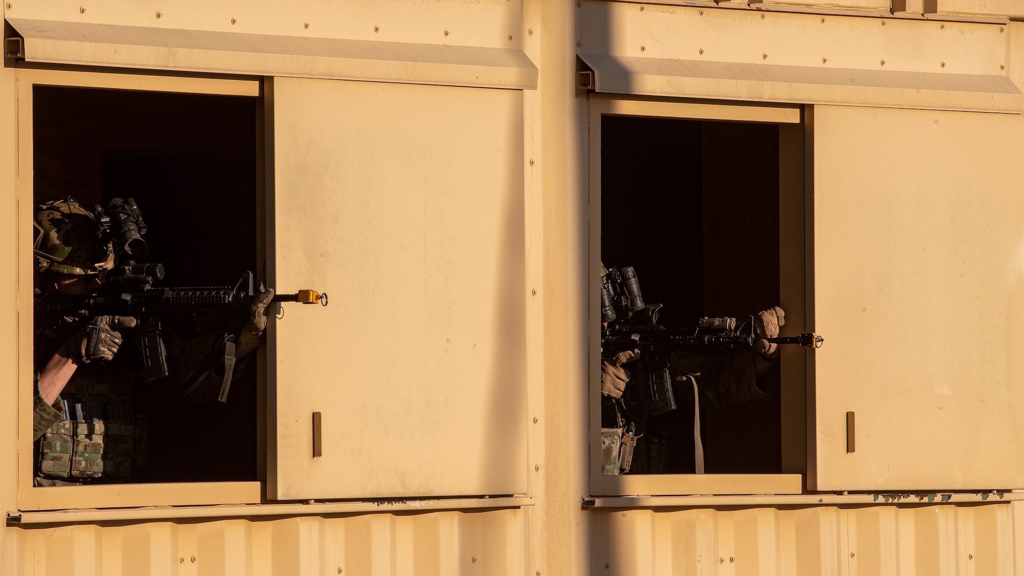 Two Airmen point rifles side-by-side windows of a metal building.