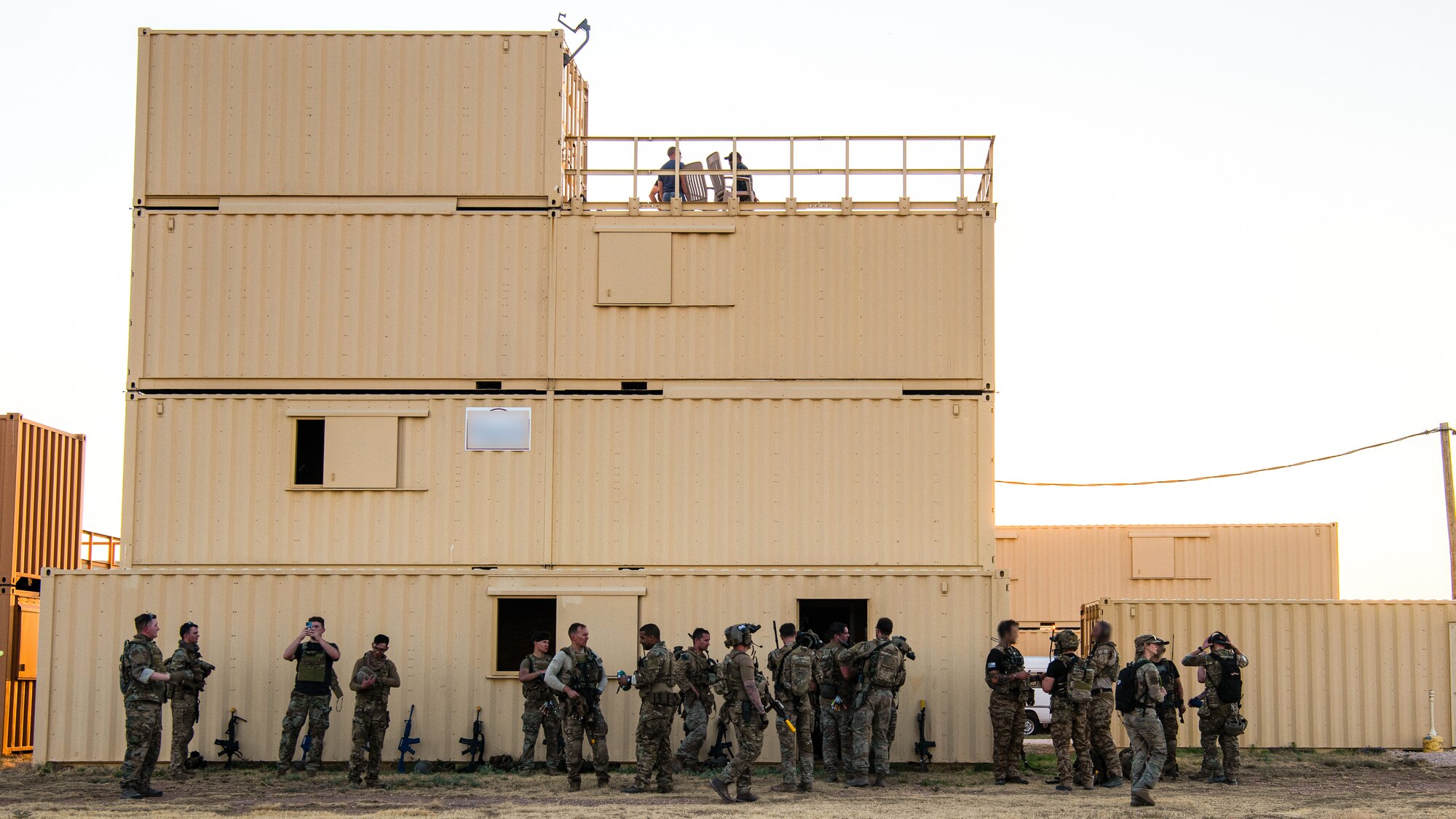 Airman and Solders gather outside of a building made out of metal conex shipping container.