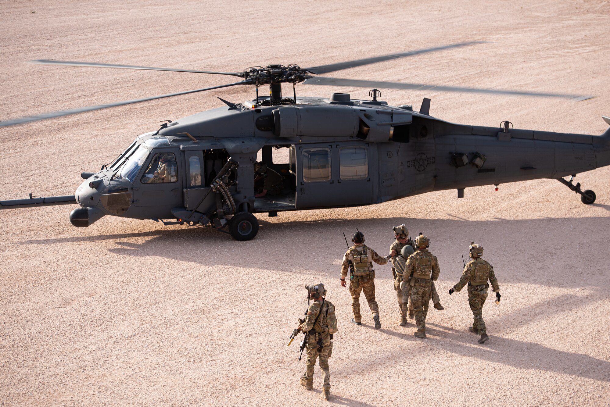 Airmen carry a simulated casualty to a helicopter while soldiers provide security for them nearby.