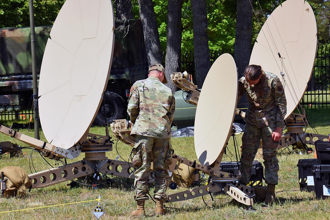 Airmen set up satellite dish-type devices in a field.