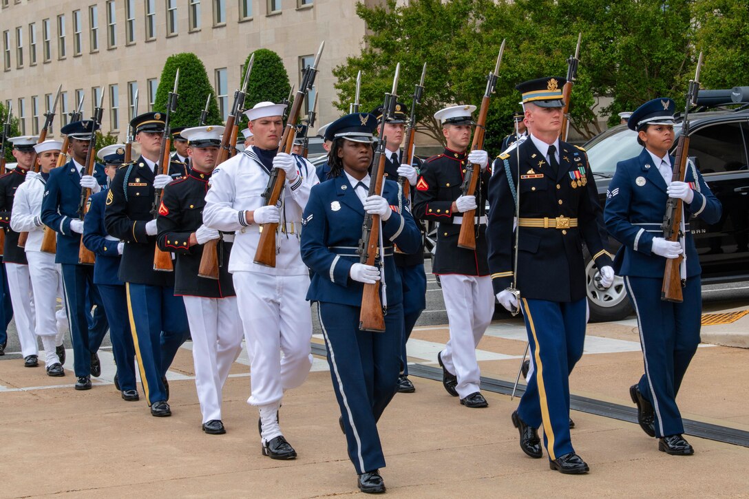 Service members from multiple branches walk in formation outside the Pentagon