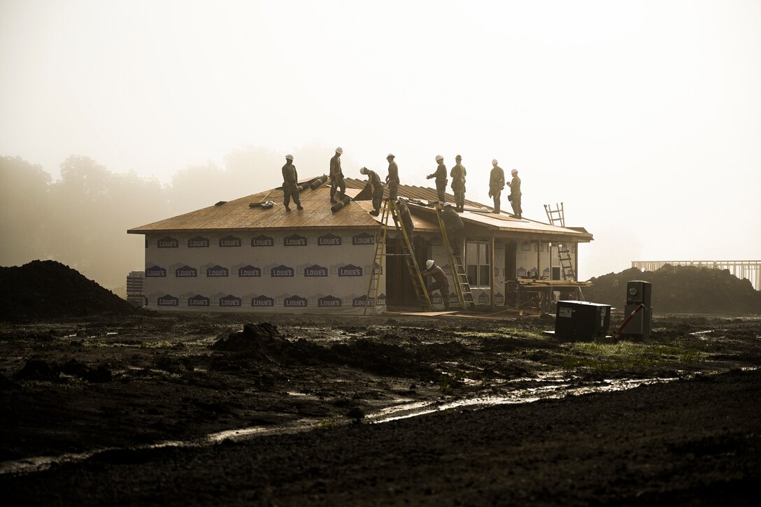 A group of people stand on the roof of a large house in a muddy area.