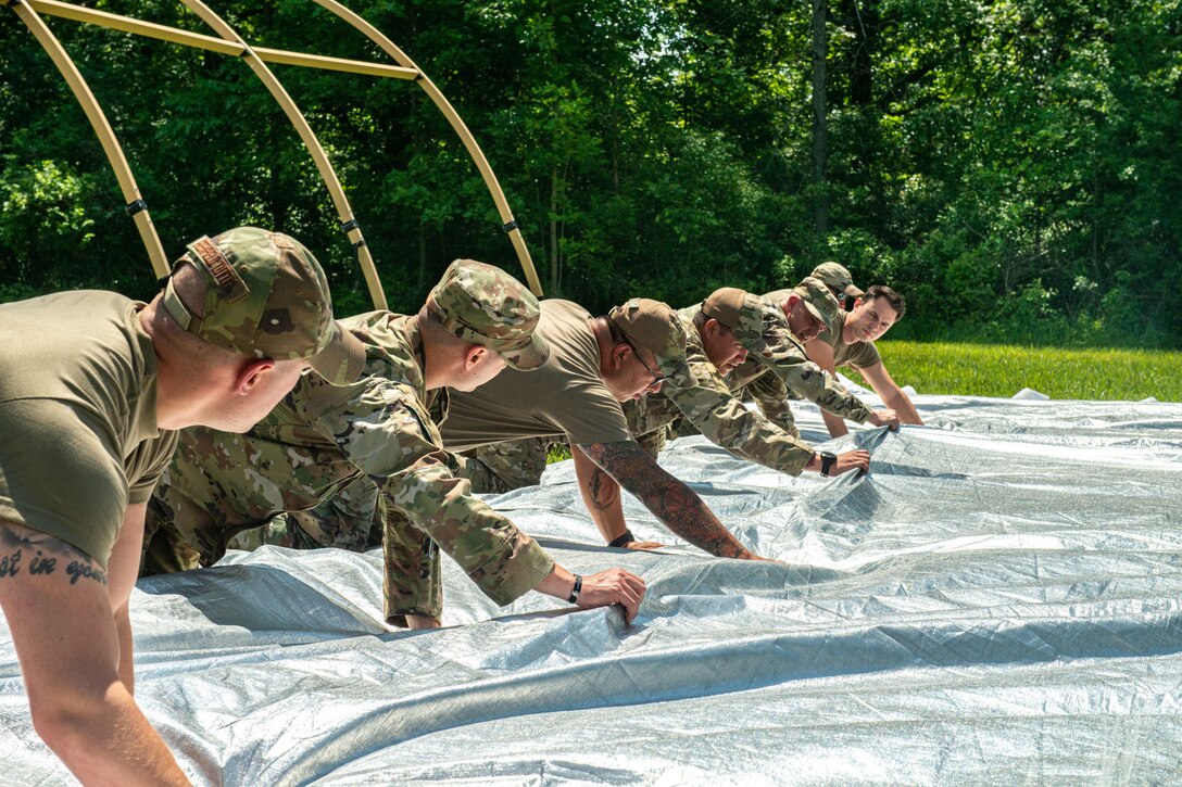 A group of airmen kneel over a large tent.
