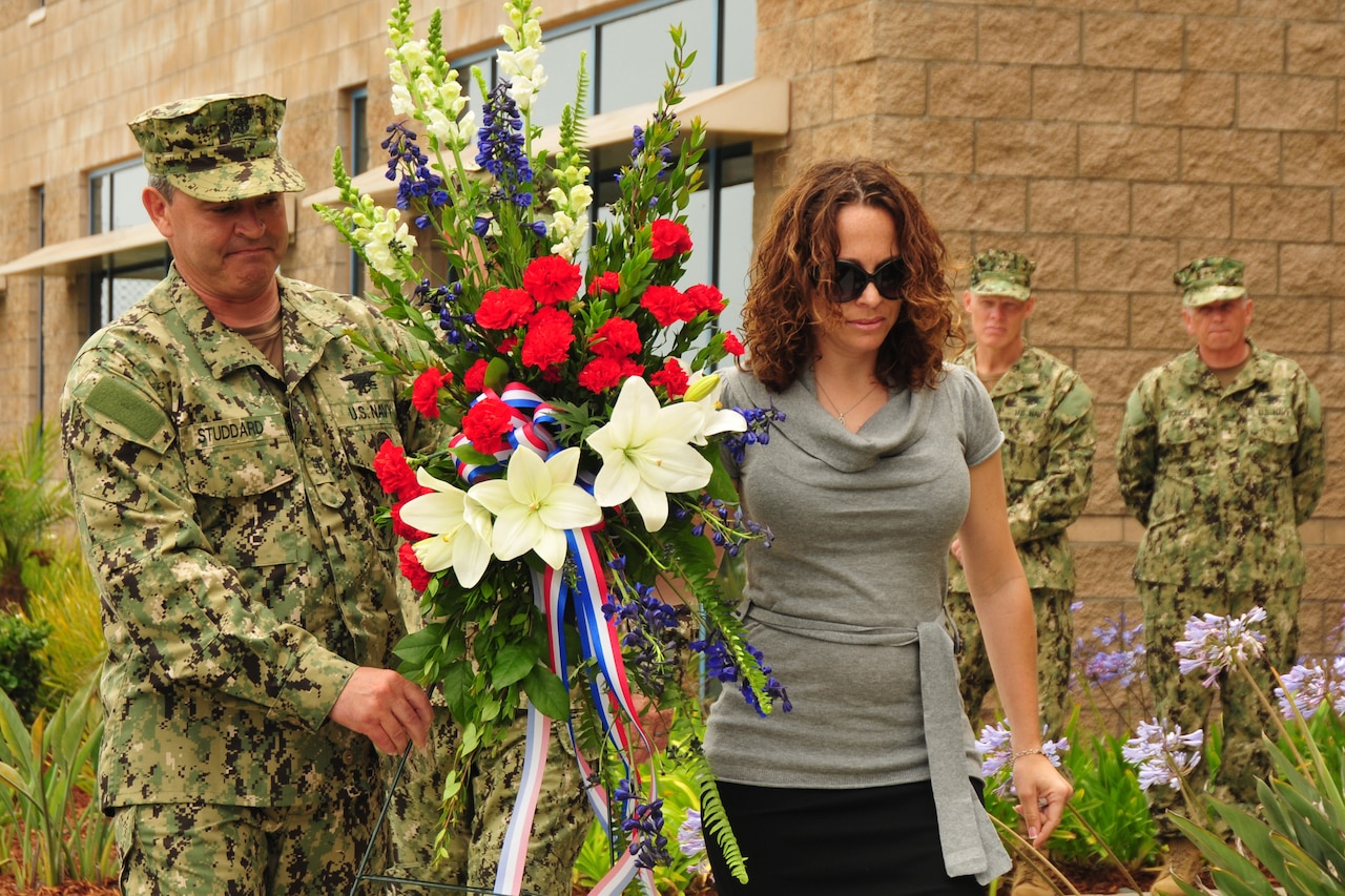 A sailor and a woman in sunglasses carry a large bouquet of flowers.