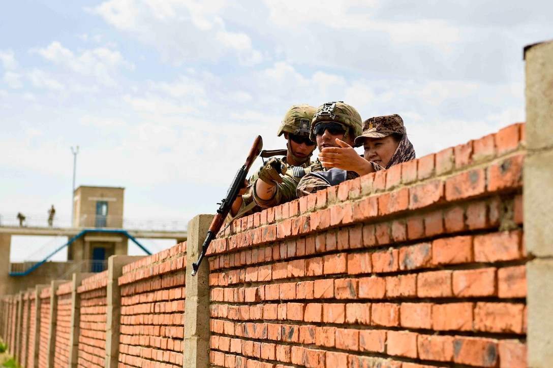 Service members stand behind a brick fence.