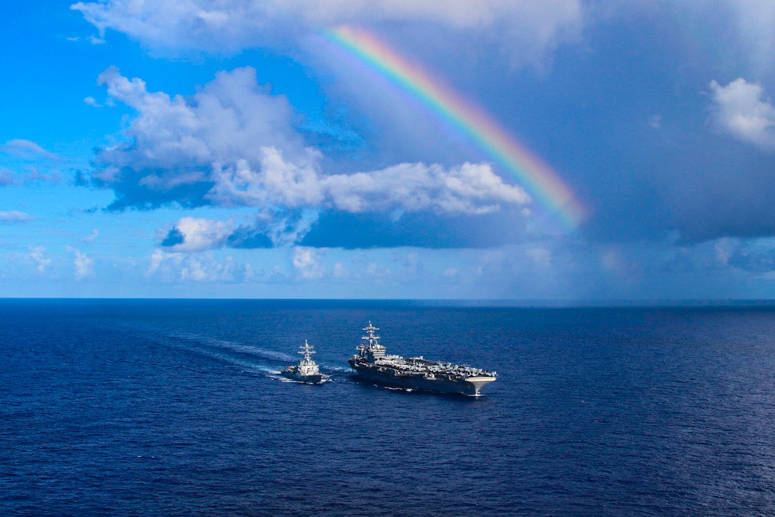 Two ships sail in waters underneath a rainbow.