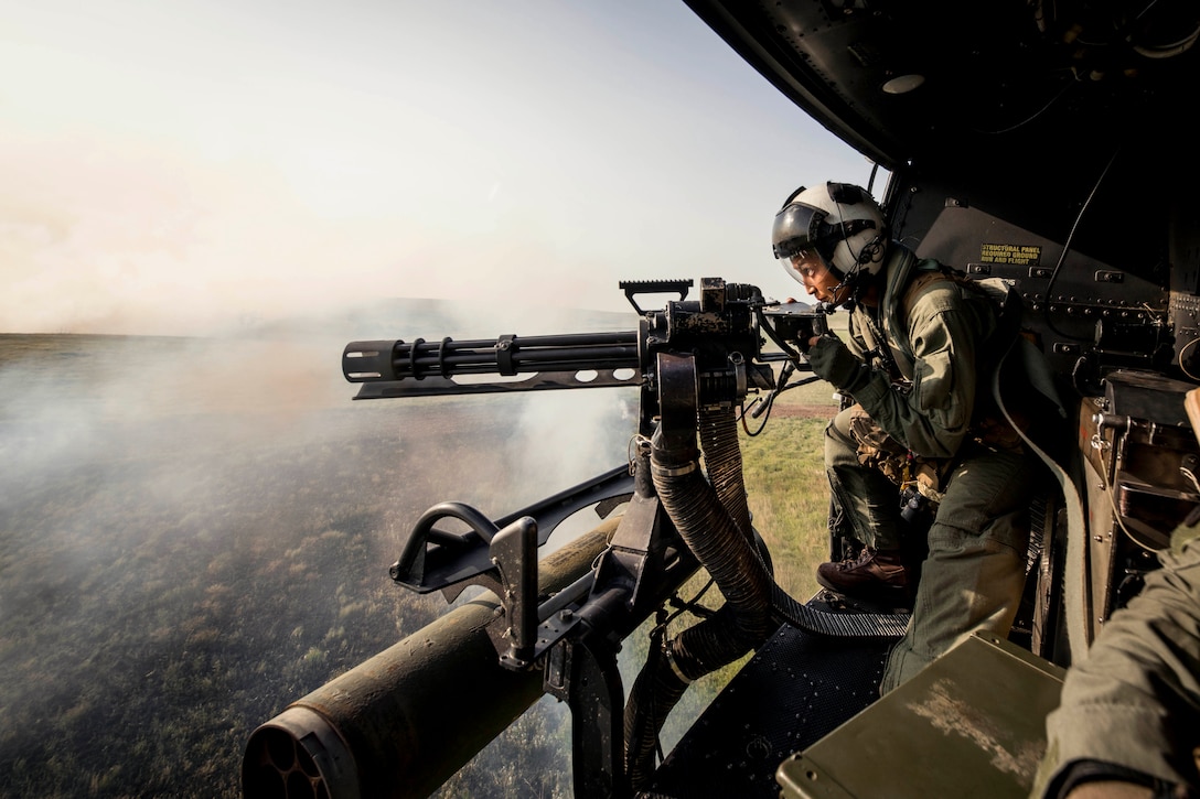 A Marine fires a weapon out of an open door of an airborne helicopter.
