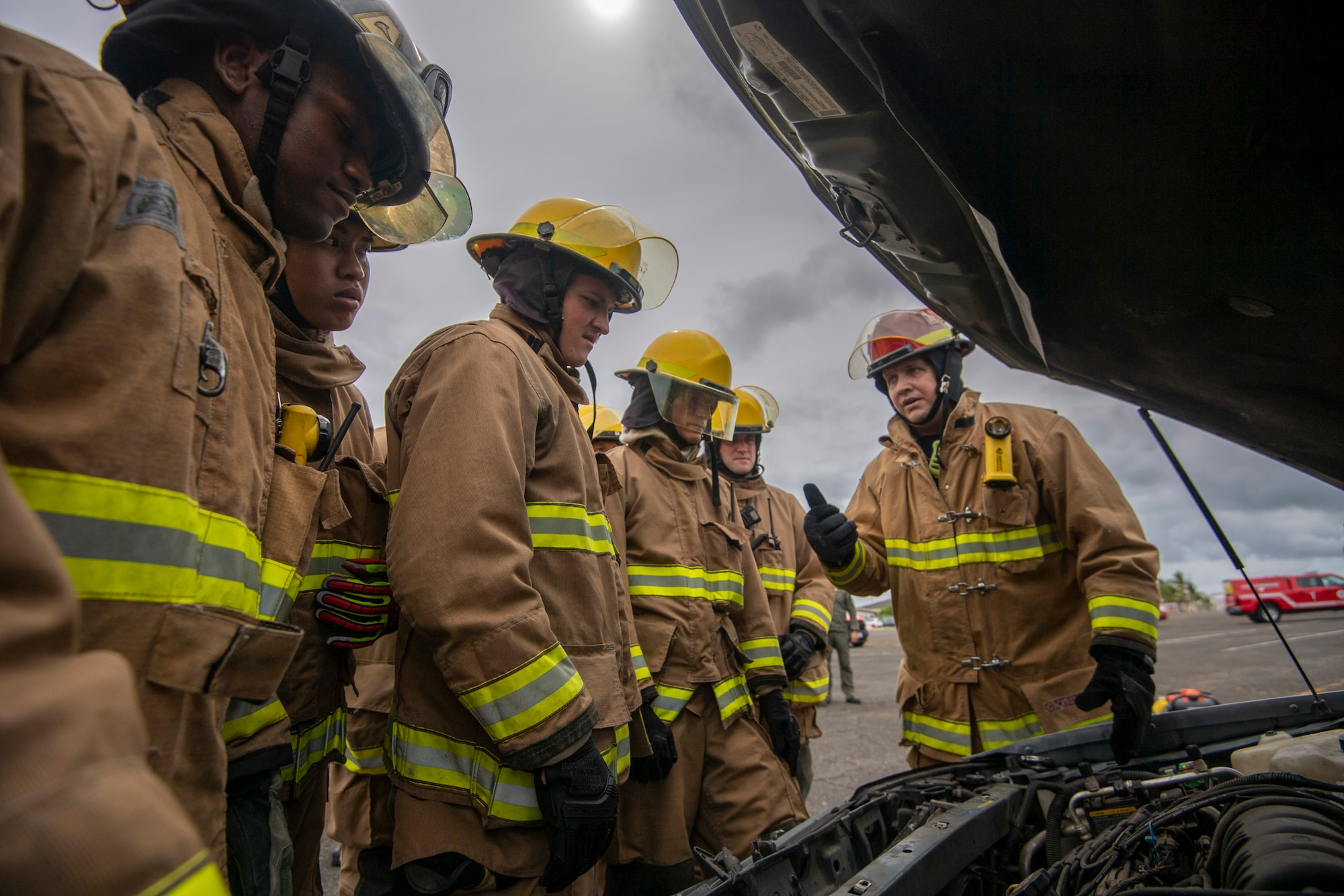 Overlooking a car engine, military members from the Air Force and Marines receive instruction on vehicle extrication wearing appropriate fire retardant PPE.
