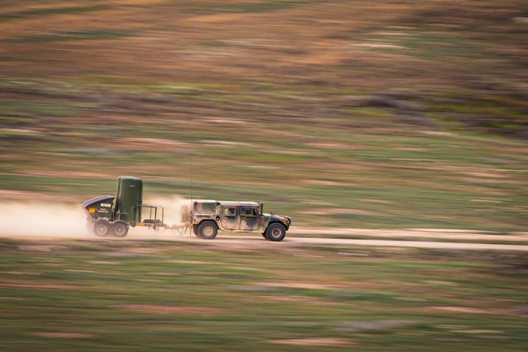 Soldiers drive a vehicle with a toilet attached to it on a dirt road.