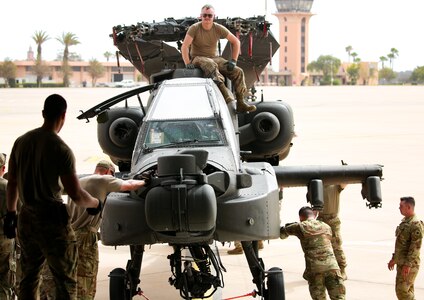 A group of soldiers push an Apache helicopter off of a C-5 Airplane.