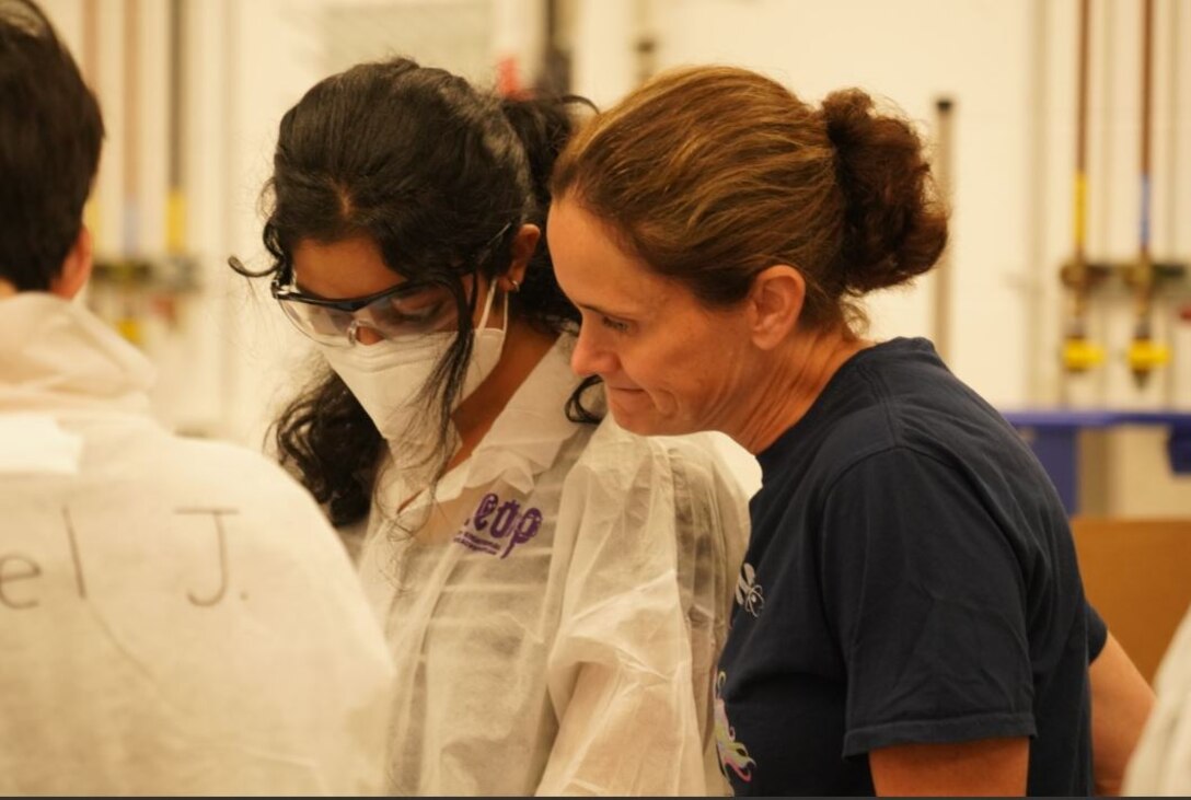 A student and an ERDC team member participate in CERL's GEMS Camp. The student wears a lab coat, mask, and safety glasses.
