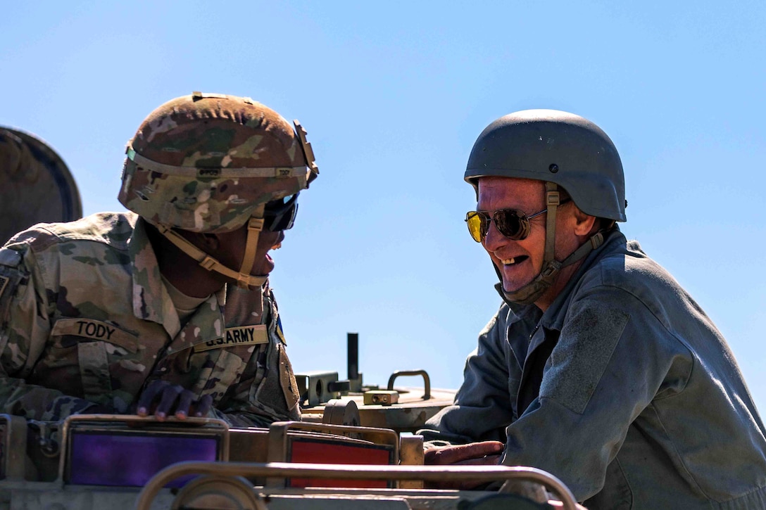 Two service members smile as they talk to each other.