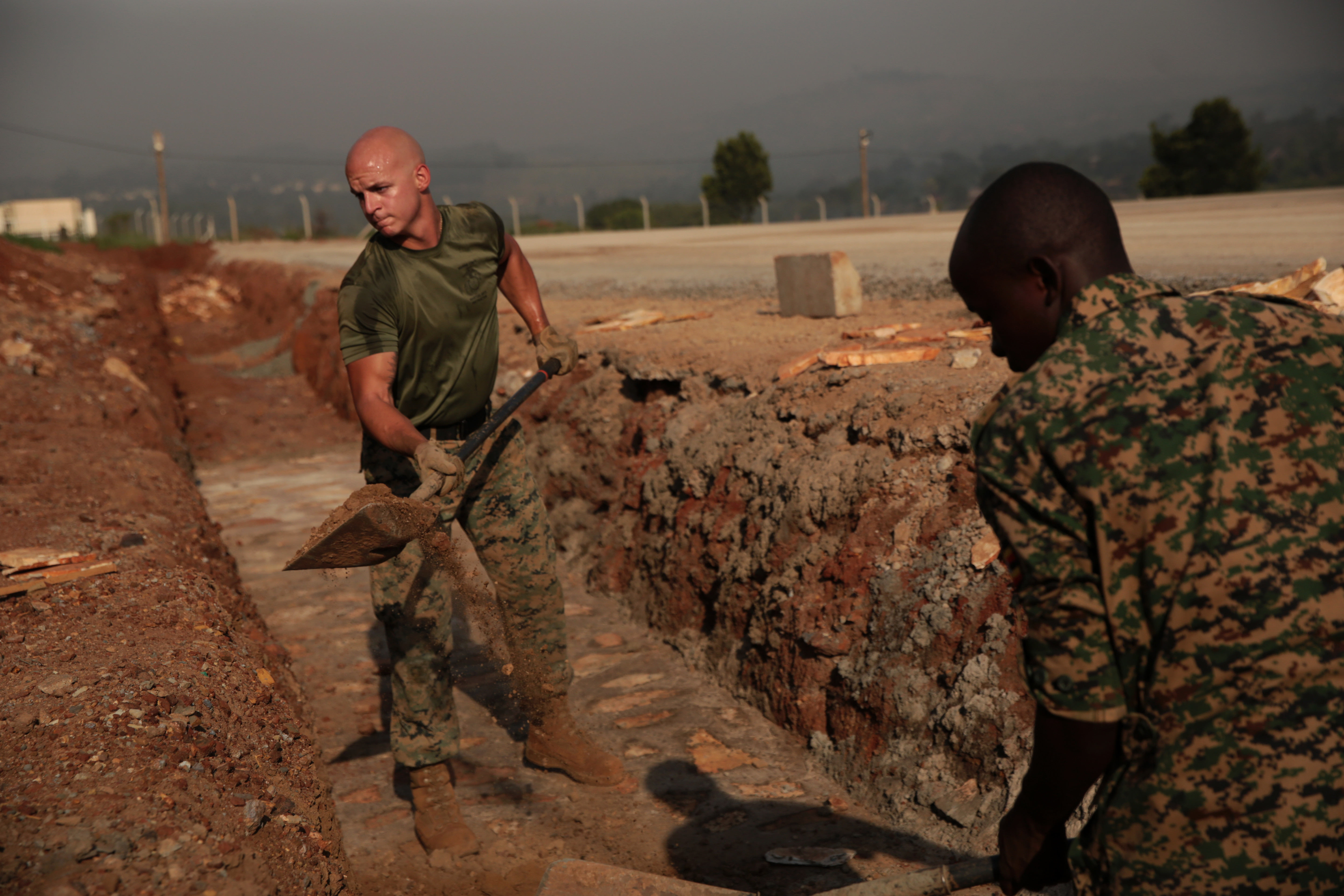 Two Marines in uniforms digging out a trench in the dirt.