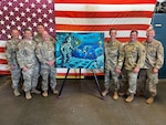 New York Air National Guard Airmen who were part of a 2017 mission to save two badly burned crewmen on board the Slovenian bulk carrier Tamar pose with a painting commemorating the mission during an awards ceremony June 4, 2022, at F.S. Gabreski Air National Guard Base in Westhampton Beach, New York.