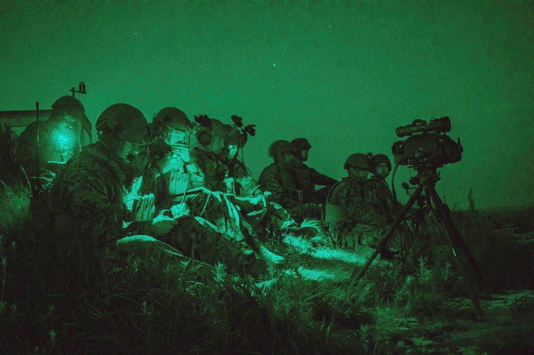 Marines illuminated by green light sit as a group.