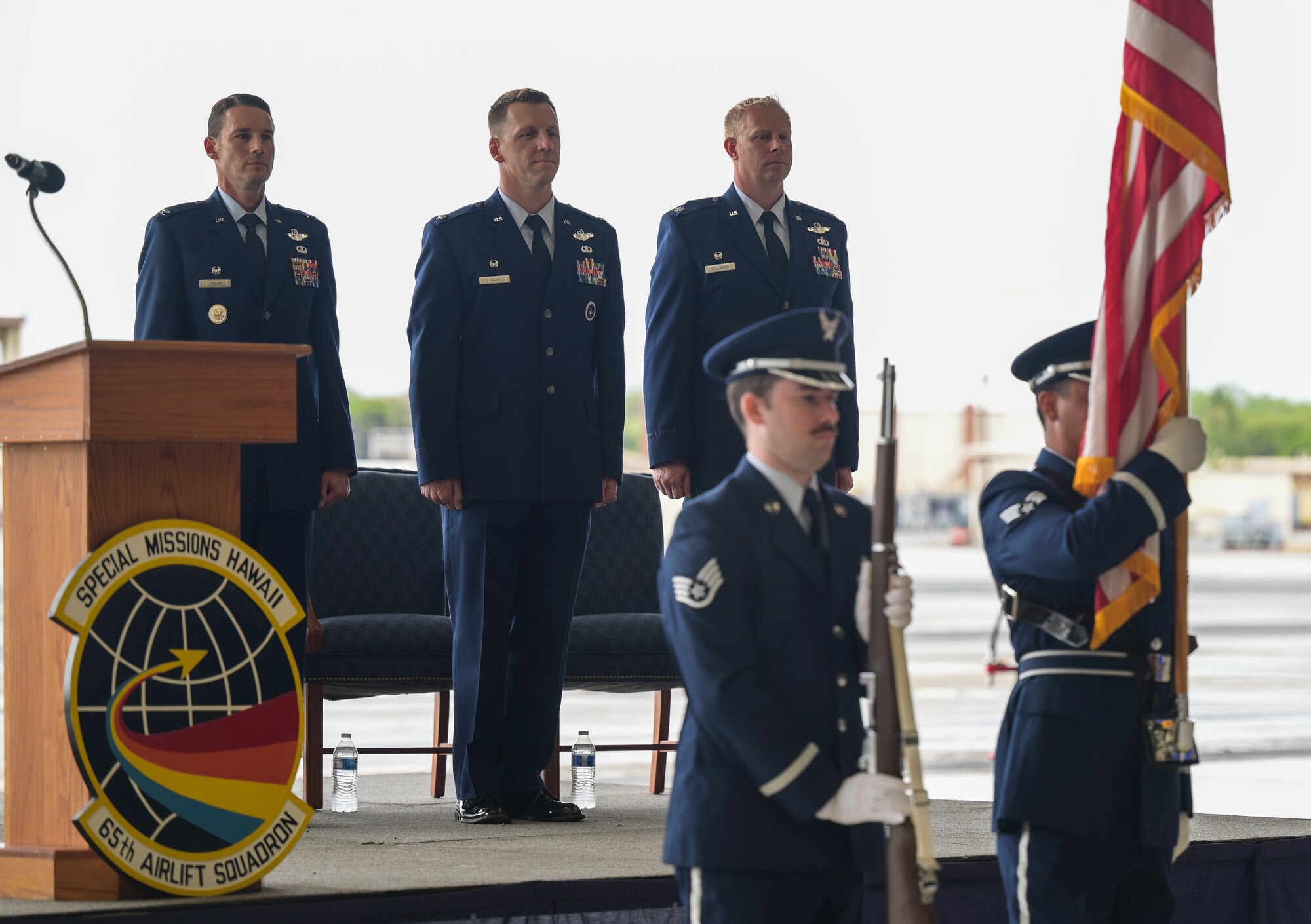 Col. Garrett Fisher, 15th Operations Group commander, Lt. Col. Matthew Hood, 65th Airlift Squadron outgoing commander, and Lt. Col. Daniel Hellinger, 65th AS incoming commander, stand at attention during the presentation of the colors at Joint Base Pearl Harbor-Hickam, Hawaii, June 24, 2022. During the ceremony, a guidon is passed from the former commander to the new commander, representing the transfer of responsibility. (U.S. Air Force photo by Staff Sgt. Alan Ricker)