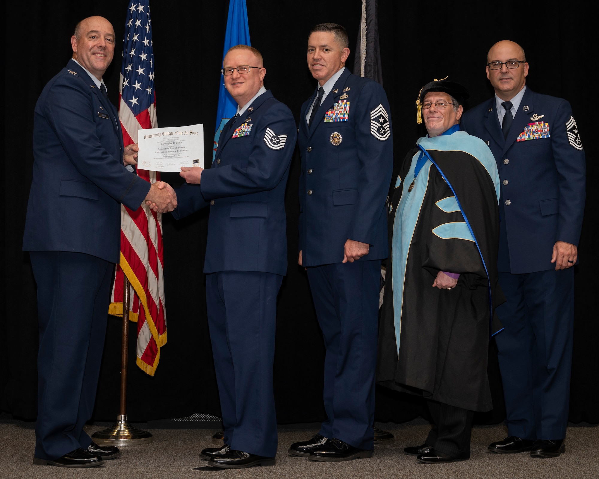 Col. Patrick Miller, 88th Air Base Wing and installation commander, presents Tech. Sgt. Christopher Tracy with his associate in applied science degree in information systems technology during the Community College of the Air Force graduation ceremony June 15, 2022, at the National Museum of the Air Force, Wright-Patterson Air Force Base, Ohio. With Miller were Jason Schaffer, 88 ABW command chief; Donald Ellwood, CCAF Education Services director; and Chief Master Sgt. James Fitch, Air Force Research Laboratory command chief; who gave the commencement address. (U.S. Air Force photo by R. J. Oriez)