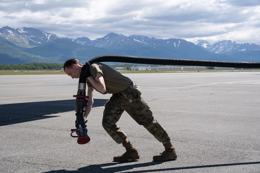 An Airman drags a large fuel hose.