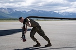 An Airman drags a large fuel hose.