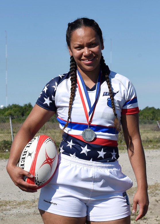 A female poses for a photo holding a rugby ball.