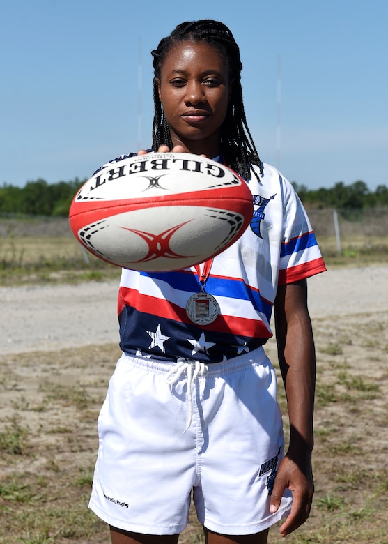 A black female holds a rugby ball toward the camera.