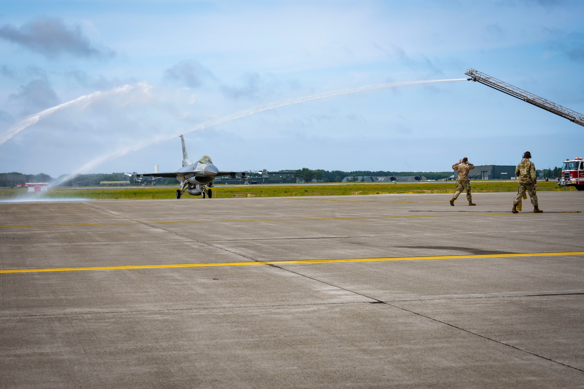 A F-16 Fighting Falcon taxis on a flight line as water gets spayed on each side of it.