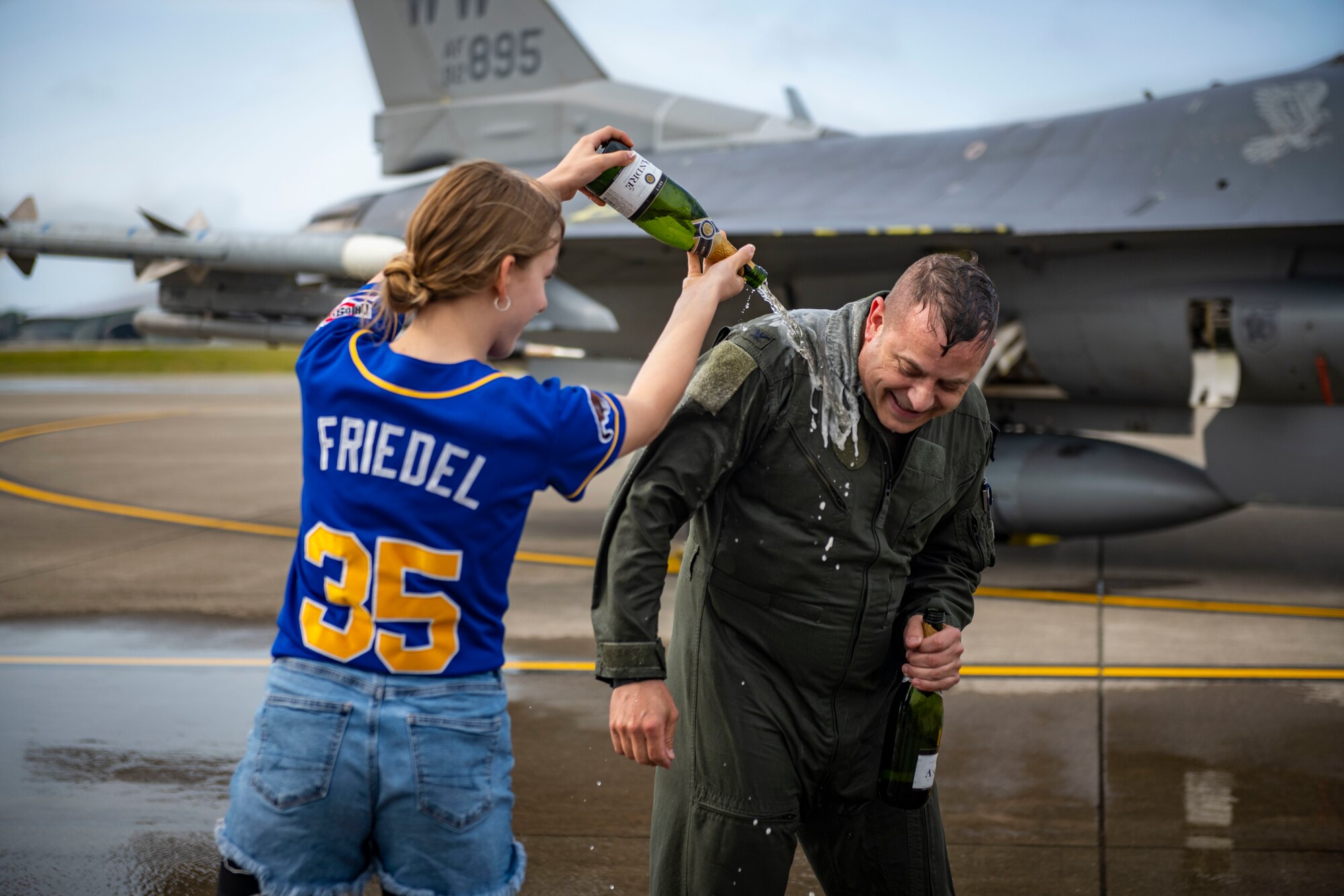 U.S. civilian dumps a bottle of champagne onto a U.S. military member in uniform.
