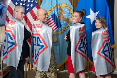 Four people stand together wearing shiny capes