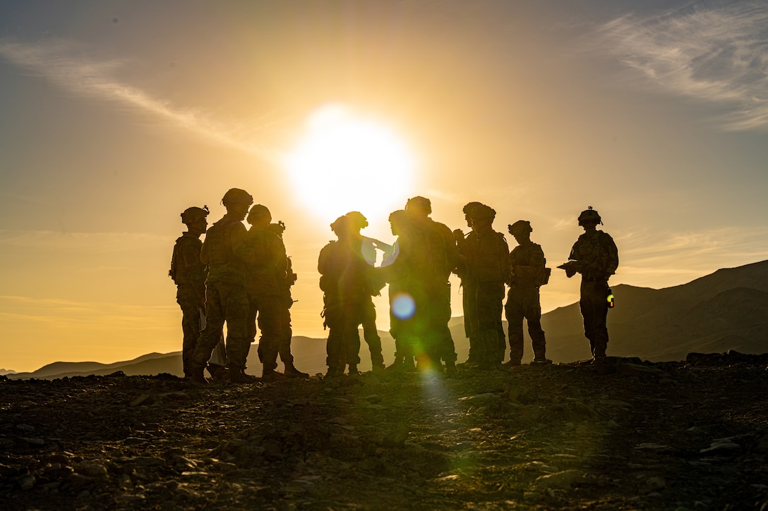 A group of soldiers gather at twilight in a mountainous area.