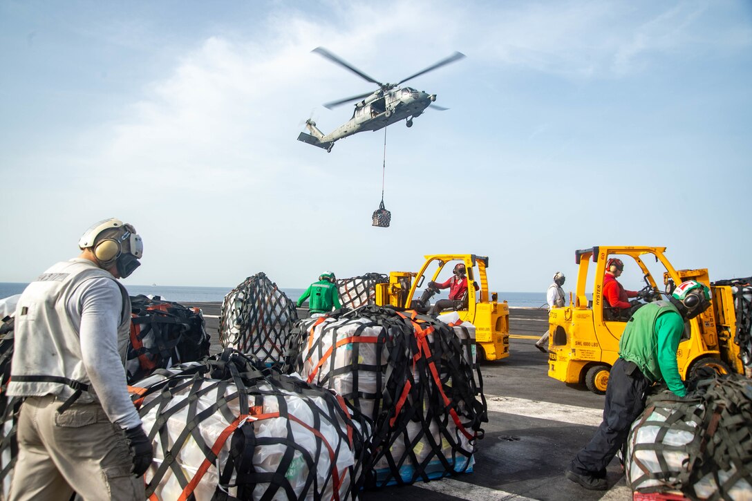 Sailors move large bundles of food on an aircraft carrier.