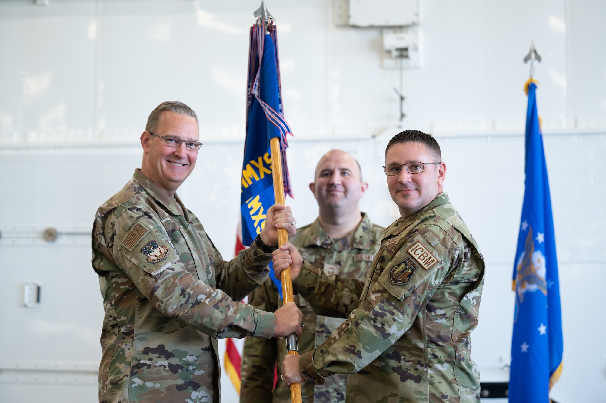 Maj. Daniel Foster, right, accepts command of the 341st Missile Maintenance Squadron from Col. Kenneth Benton, left, 341st Maintenance Group commander, while Senior Master Sgt. Brian Brown, 341st MMXS first sergeant, looks on, during a change of command ceremony June 24, 2022, at Malmstrom Air Force Base, Mont.