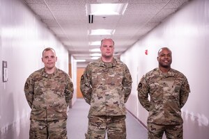 Three airmen from the Contracting Training Flight pose in a hallway