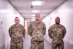 Three airmen from the Contracting Training Flight pose in a hallway