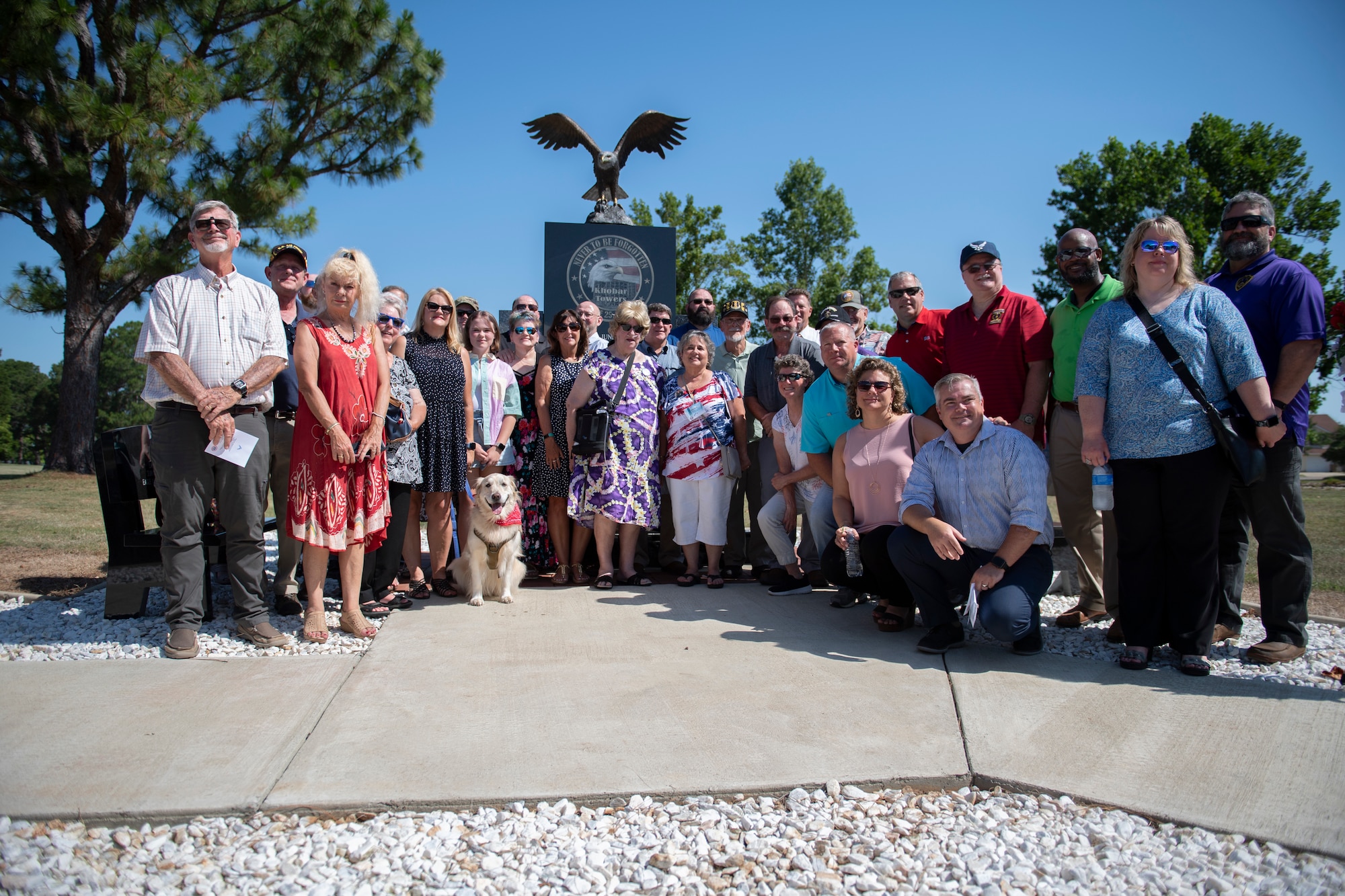 A photo of a group of people standing and kneeling in front of a monument that has an eagle on top of it.