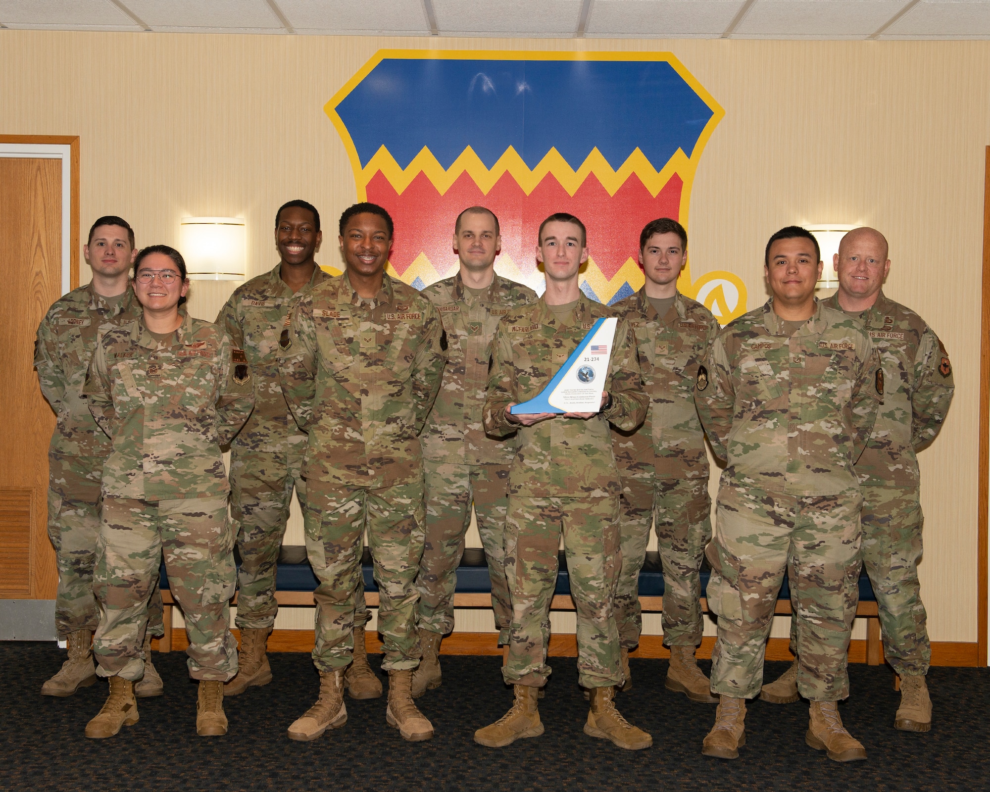 men and women in uniform pose for a photo in front of the 55th Wing shield. One person holds the award.