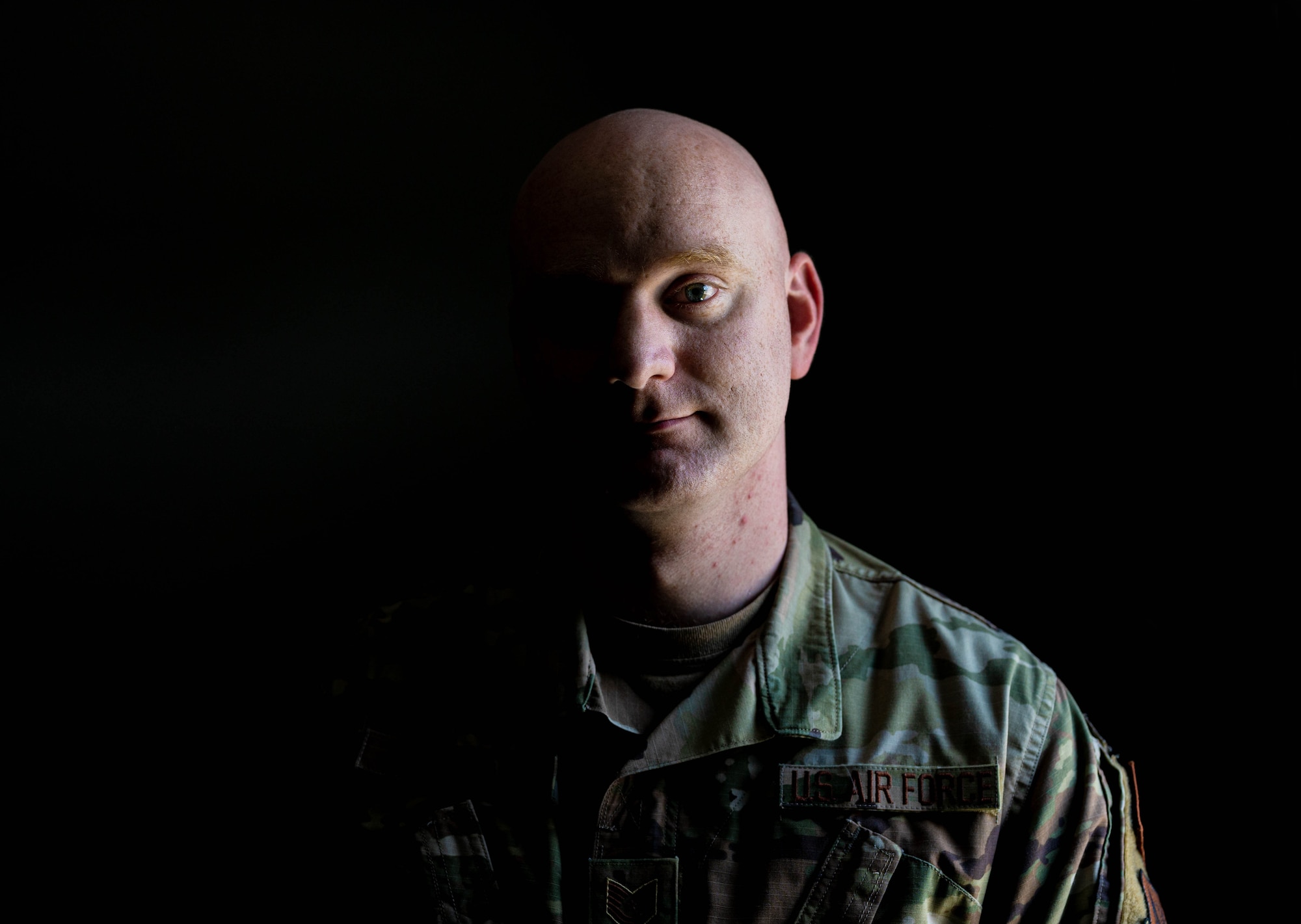 An Airman poses for a photo in a dark room with light shining on one half of his face