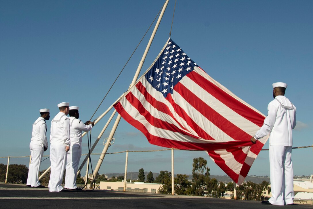 Sailors hold an American flag aboard a ship at sea.