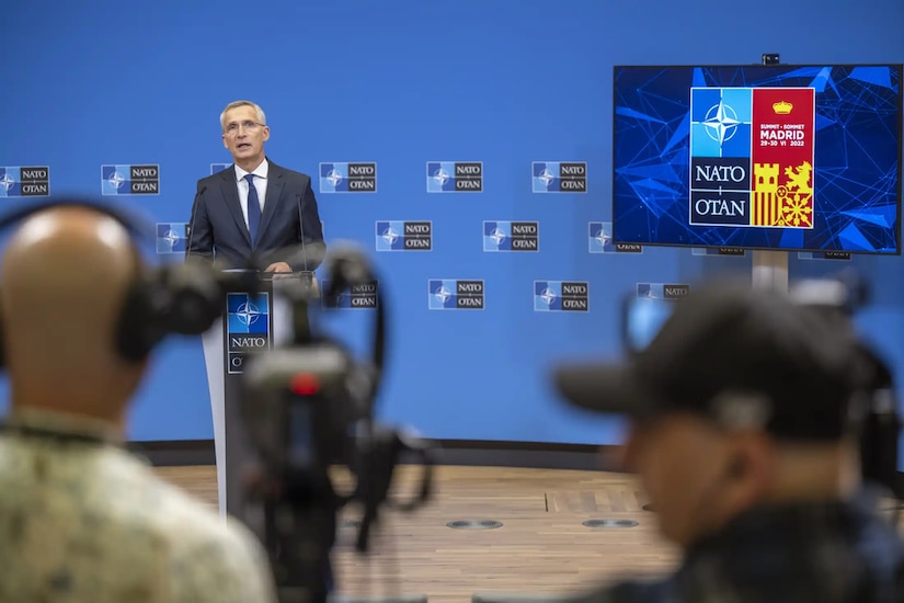 A man stands behind a lectern with a sign that says NATO and addresses the media.